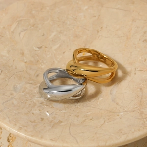 Polished gold and silver geometric criss-cross rings on a beige marble display plate