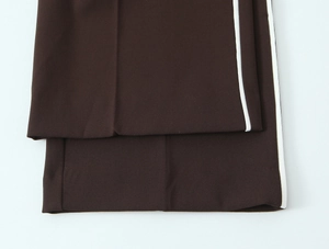 Detail of dark brown straight trousers featuring white side stripes and fine fabric texture