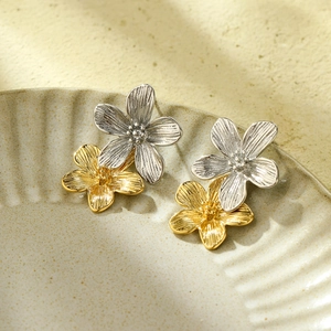 Detail of layered gold and silver floral earrings with brushed metallic texture on ceramics