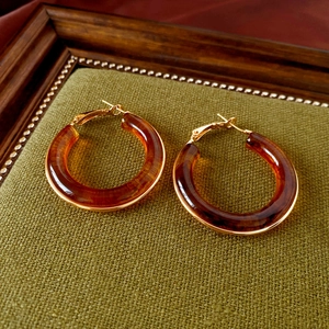 Detail view of large amber resin hoop earrings with gold metal frame on a green stand