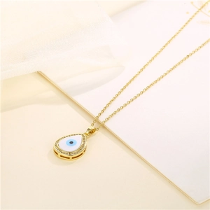 Elegant gold teardrop evil eye necklace with micro-pave crystals on soft beige fabric
