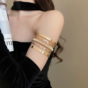 Detail showing five stacked gold metallic bracelets with wave and textured designs on a model