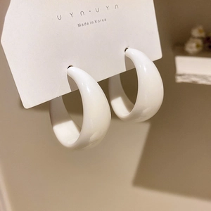 Close-up of white resin C-shaped hoop earrings with a glossy finish on brand card