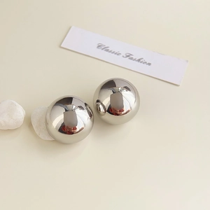 Detailed view of polished 18K silver geometric sphere stud earrings on beige background