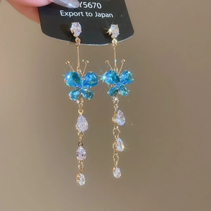 Macro shot of blue crystal butterfly earrings with sparkling tassel and gold chain detailing