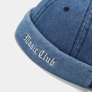 Gros plan sur la broderie Basic Club blanche sur le denim bleu marine du bonnet