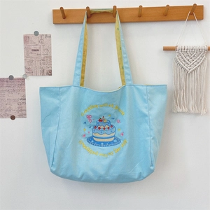 Close-up of canvas tote bag featuring cake embroidery and positive text design