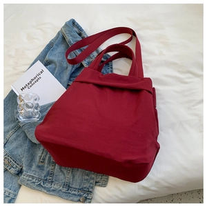Flat lay of a red nylon tote bag with reinforced handles and lifestyle props