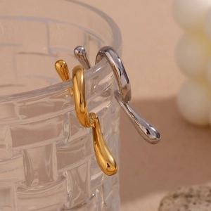 Detailed shot of irregular liquid-style gold and silver earrings on a glass rim
