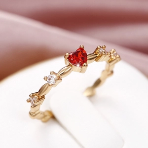 Macro detail of elegant gold ring featuring a heart-shaped red gemstone and side crystals