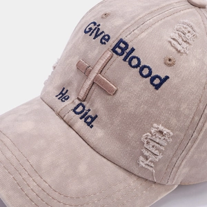 Detail of embroidered cross and text on washed cotton baseball cap with distressed texture