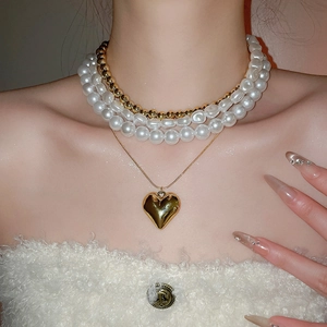 Détail des colliers superposés en perles et or avec un pendentif en cœur poli