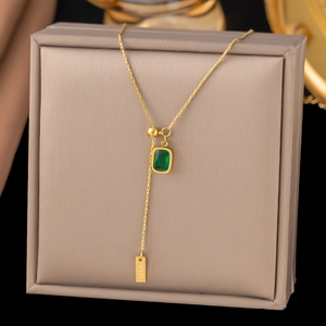 Detail view of a gold titanium steel necklace with a green rectangular gemstone and BABY tag
