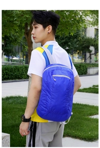 Outdoor model wearing a lightweight blue foldable backpack showing side zipper and grey straps