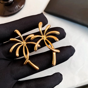 Macro shot of gold-plated palm tree earrings held by a black gloved hand showing fine detail