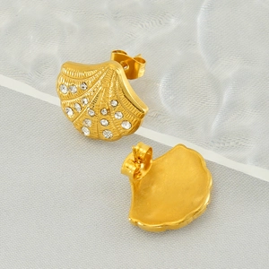 Detailed close-up of gold shell-shaped earrings with sparkling diamonds on grey fabric