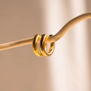 Chunky golden stainless steel hoop earrings with polished finish on a wooden branch