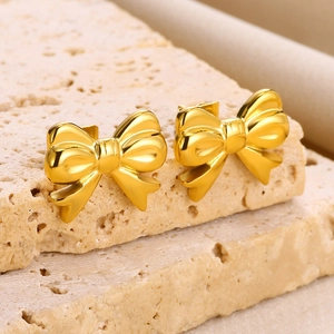 Detailed close-up of 18K gold-plated bow stud earrings on a textured stone display