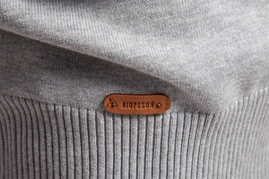 Detailed view of grey knit texture and brown leather brand label on men's sweater