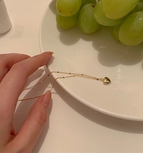 Detailed view of the gold heart pendant necklace held over a plate with fresh green grapes