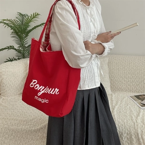 Detail of red canvas tote bag with Bonjour print worn with a white shirt and grey skirt