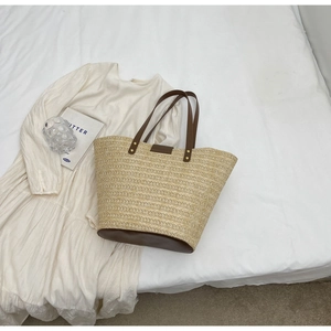Flat lay of straw tote bag with brown PU handles and base on white aesthetic fabric