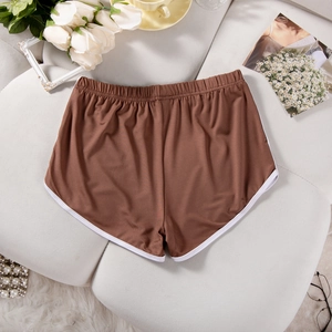 Detailed close-up of brown elastic yoga shorts with white piping on a grey sofa