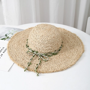Handmade raffia sun hat with wide brim and leaf pattern ribbon on a white table