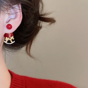Détail de clous rouges et boucles d'oreilles cheval à bascule doré avec cristaux