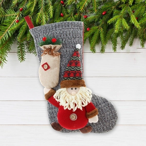 Knitted grey Christmas stocking with Santa doll and linen gift bag on white wood background
