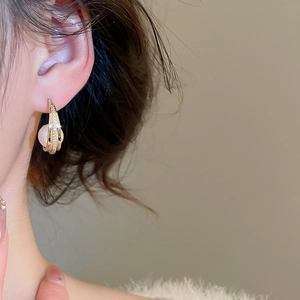 Close-up of gold C-shaped pearl earring with zircons worn on model's ear