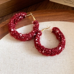 Detailed macro shot of red plush hoop earrings on a warm textured linen background
