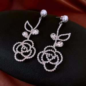 Detail of rose drop earrings with pavé crystals and pearl on black display stand