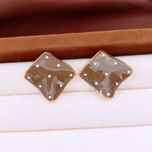 Macro shot of brown rhombic stud earrings with white polka dots and gold metal edges