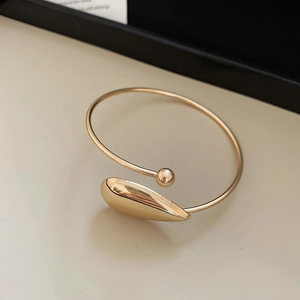 Detailed close-up of a golden open bangle bracelet with a smooth waterdrop design