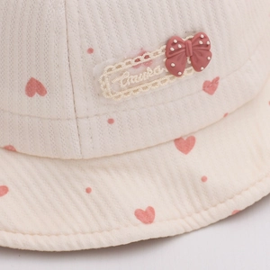Détail du chapeau pour bébé en coton crème avec imprimés cœurs roses et nœud décoratif