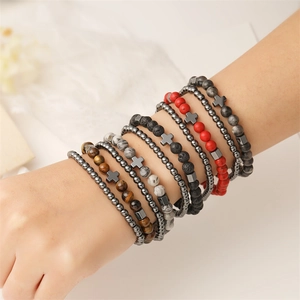 Close-up of stacked beaded bracelets with natural stones and metal cross on model arm
