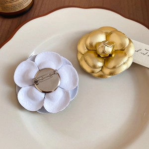 Detailed view of camellia flower brooches in white and gold finish with pin backing