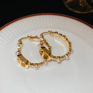 Macro shot of gold-plated pearl hoop earrings with CD motif on a white ceramic plate