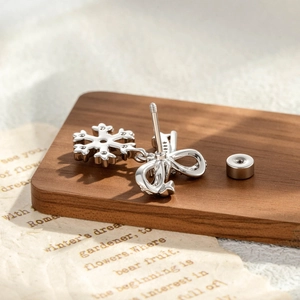 Silver snowflake and bow screw-back stud earrings on a vintage paper wood display