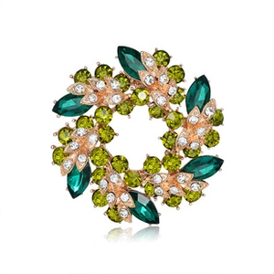 Macro view of rose gold floral brooch with green gems and crystals on white backdrop