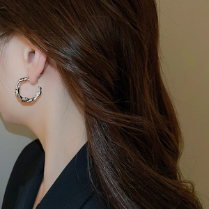 Macro view of C-shaped silver earrings with liquid lava texture on a female model
