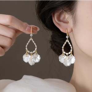 Détail de boucles d'oreilles dorées à pampilles en nacre avec zircons et pétales