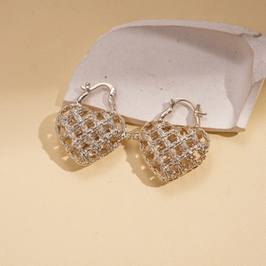 Close-up of golden hollow heart earrings with intricate woven texture on stone