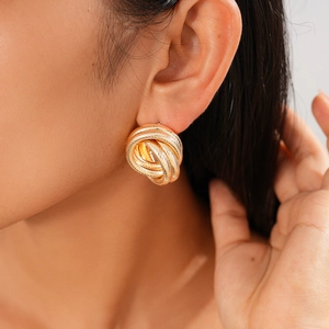 Close-up of a model wearing gold intertwined geometric hoop earrings with metallic texture
