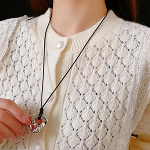 Detail of silver irregular geometric pendant on black leather cord worn over knitwear