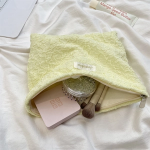 Close-up of a pale yellow pleated fabric makeup pouch with smooth metal zipper detail