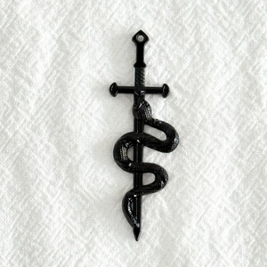 Détail d'un pendentif vintage en alliage noir représentant un serpent enroulé sur une épée