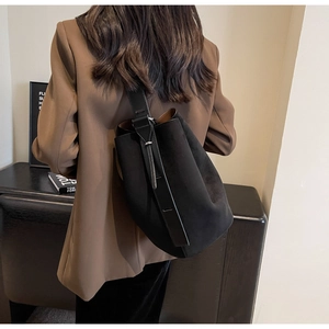Minimalist black matte bucket bag worn over the shoulder with a vintage brown suit