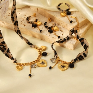 Detail of leopard print ribbon entwined with gold chain and heart pendants on stone